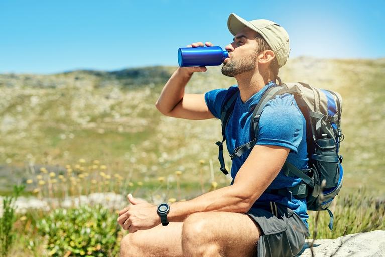 Man drinking from water bottle after hiking in the mountains.